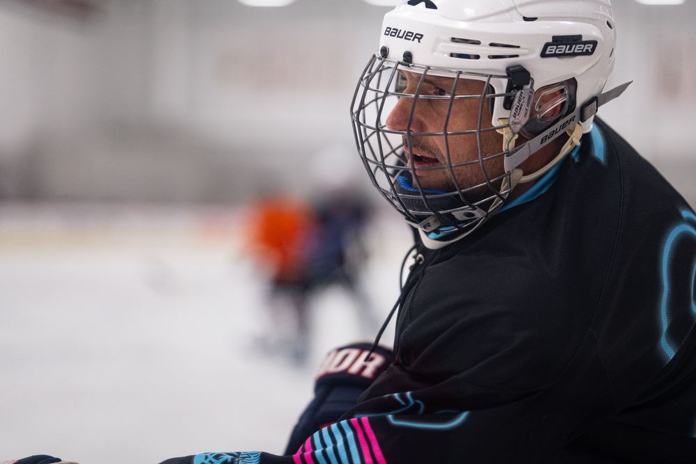 A hockey player in a black jersey and white helmet looks ahead on the ice