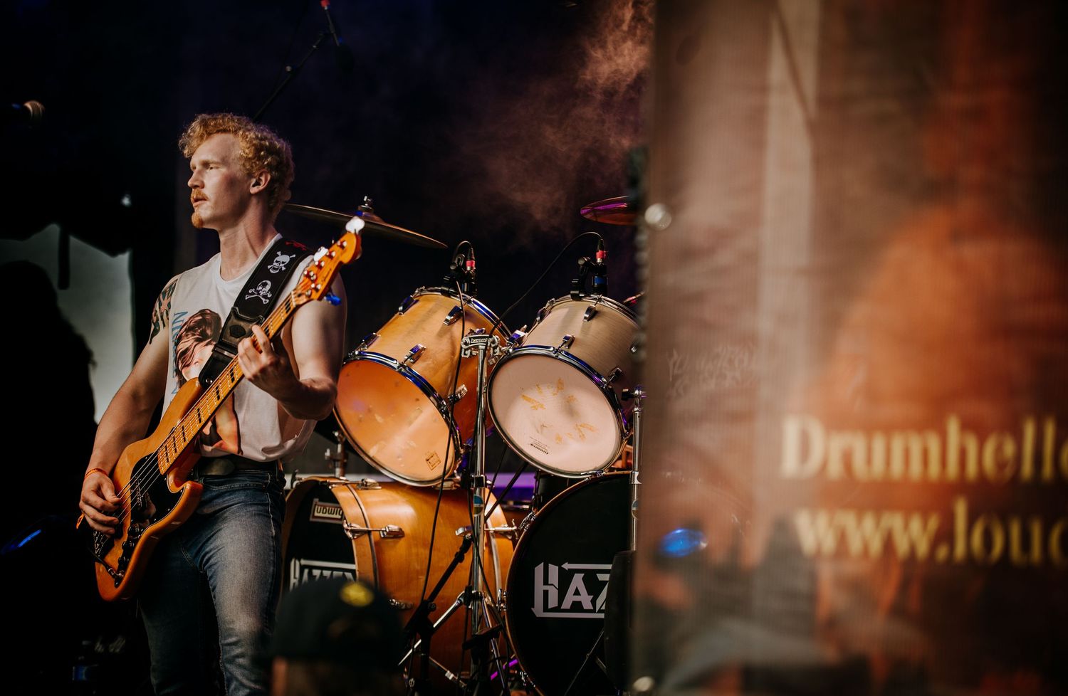 Musician performs energetically on stage with guitar and orange lighting effects during live concert.