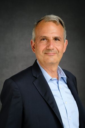 Corporate headshots of person in navy suit and light blue shirt against dark backdrop.