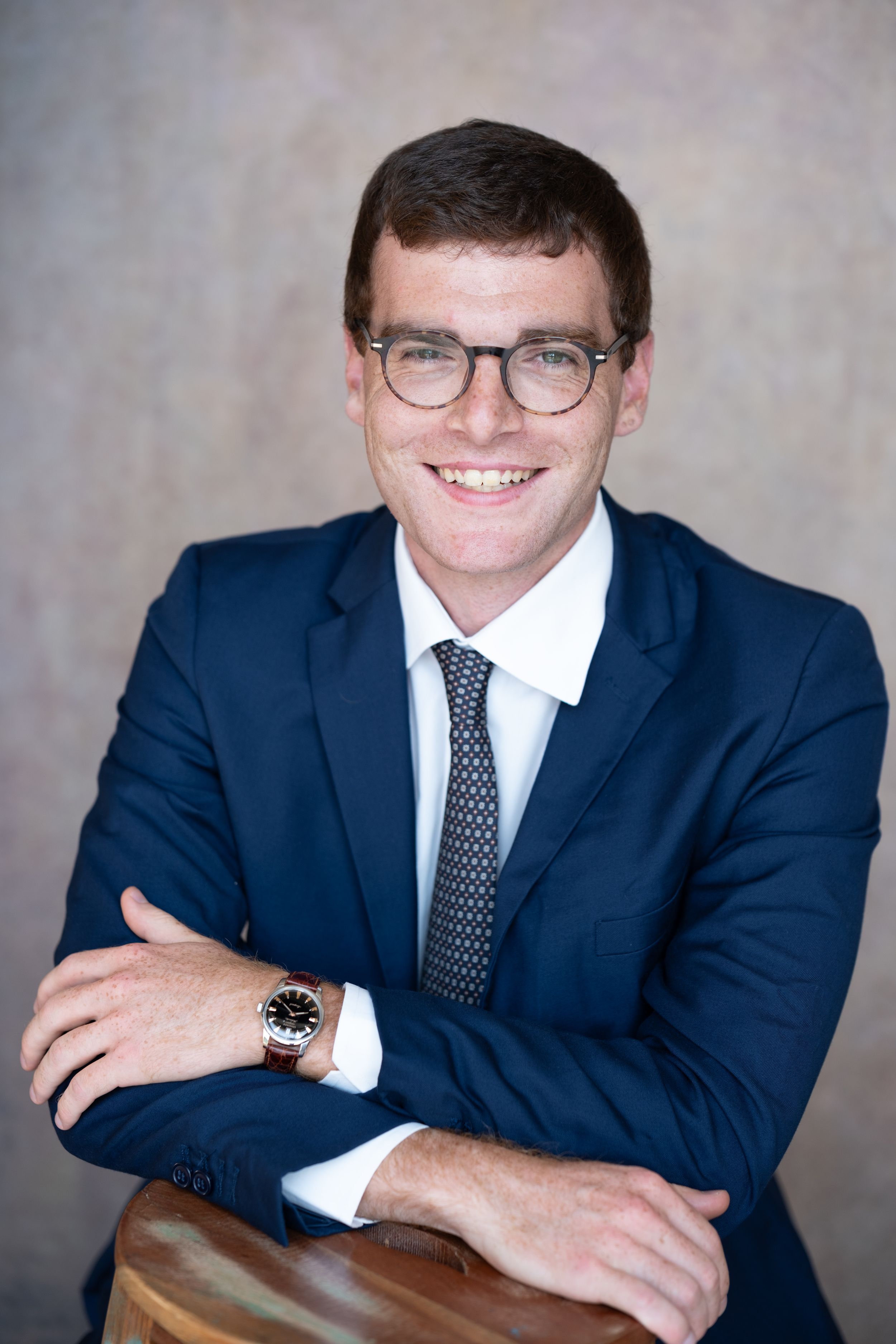 Corporate headshot series featuring navy suit, polka dot tie and glasses in professional setting.