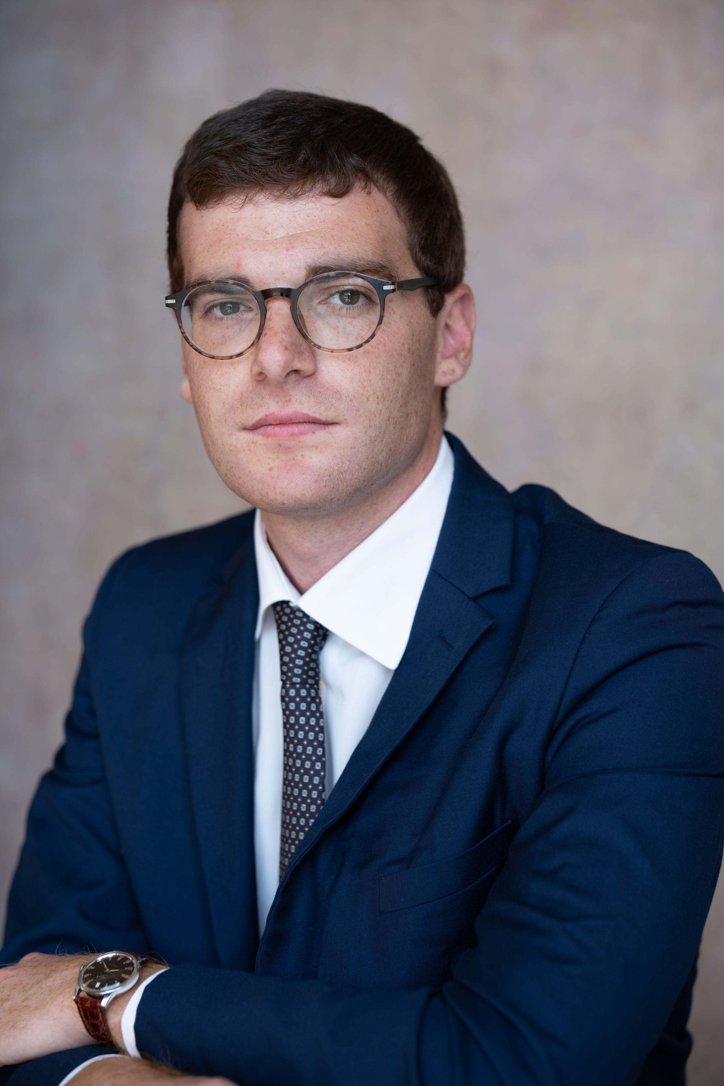 Professional headshots of person in navy suit and glasses against neutral backdrop.