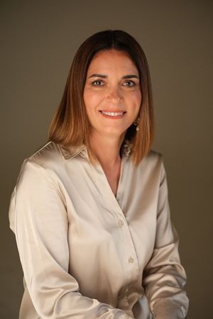 Professional headshots of person in cream colored blazer against warm background.