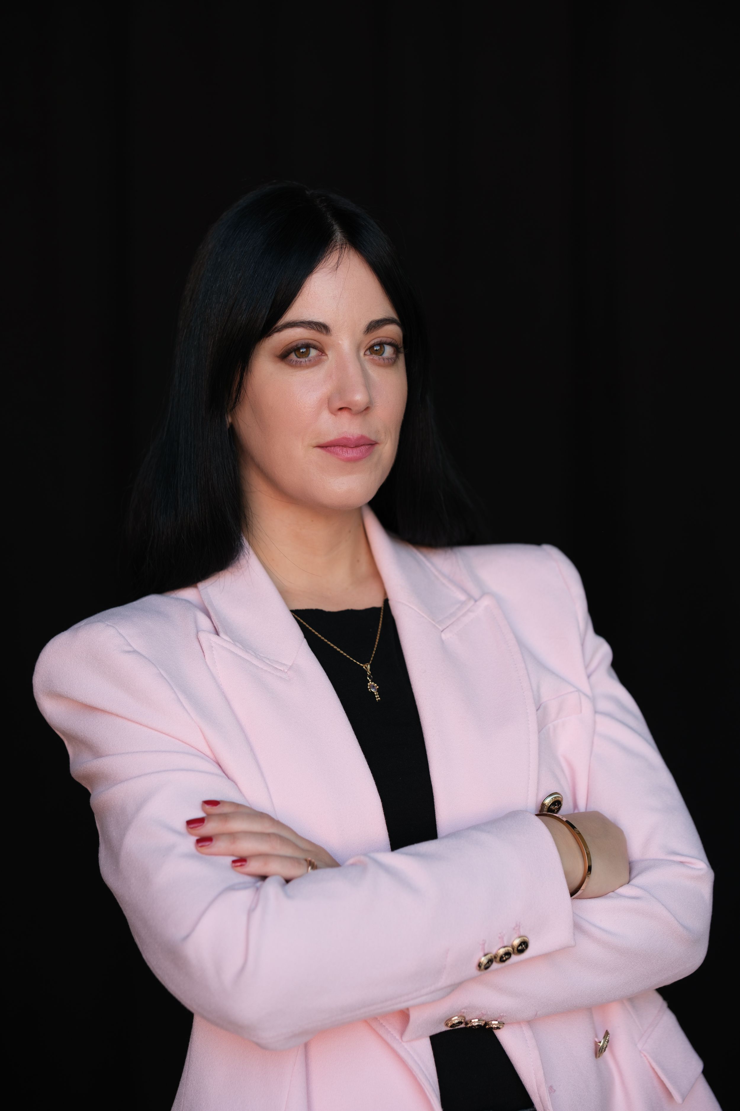 Professional portrait of someone in a light pink blazer and black top against dark background.