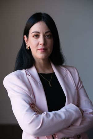 Studio portraits of person wearing pink blazer and black top with arms crossed.