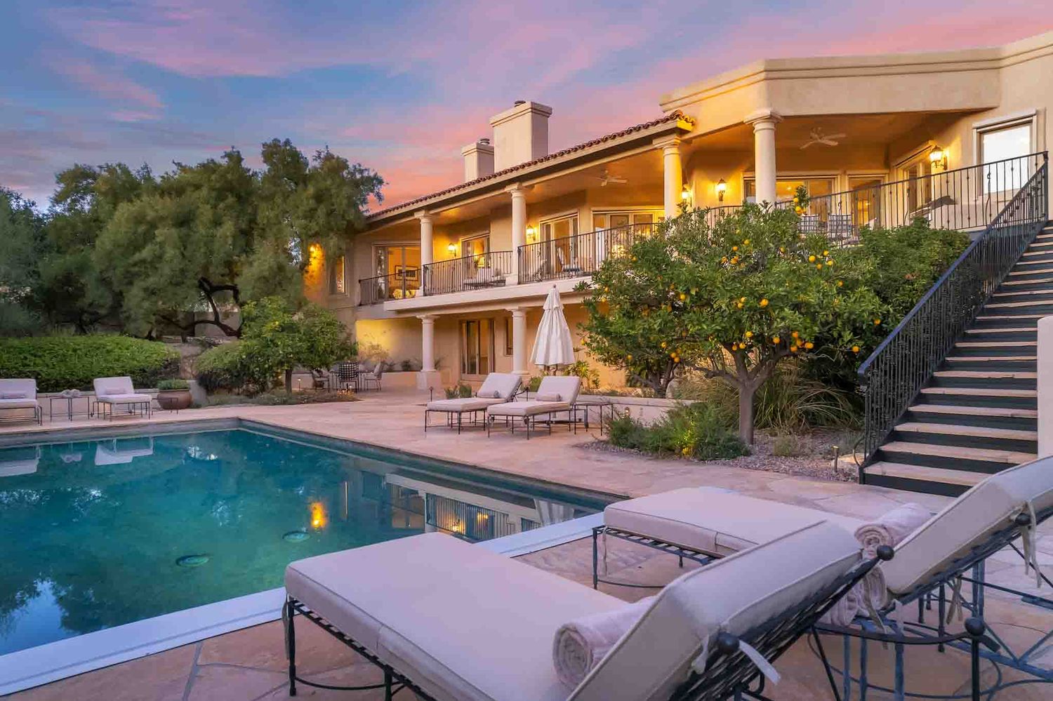 Twilight view of modern home exterior with illuminated pool and outdoor staircase.