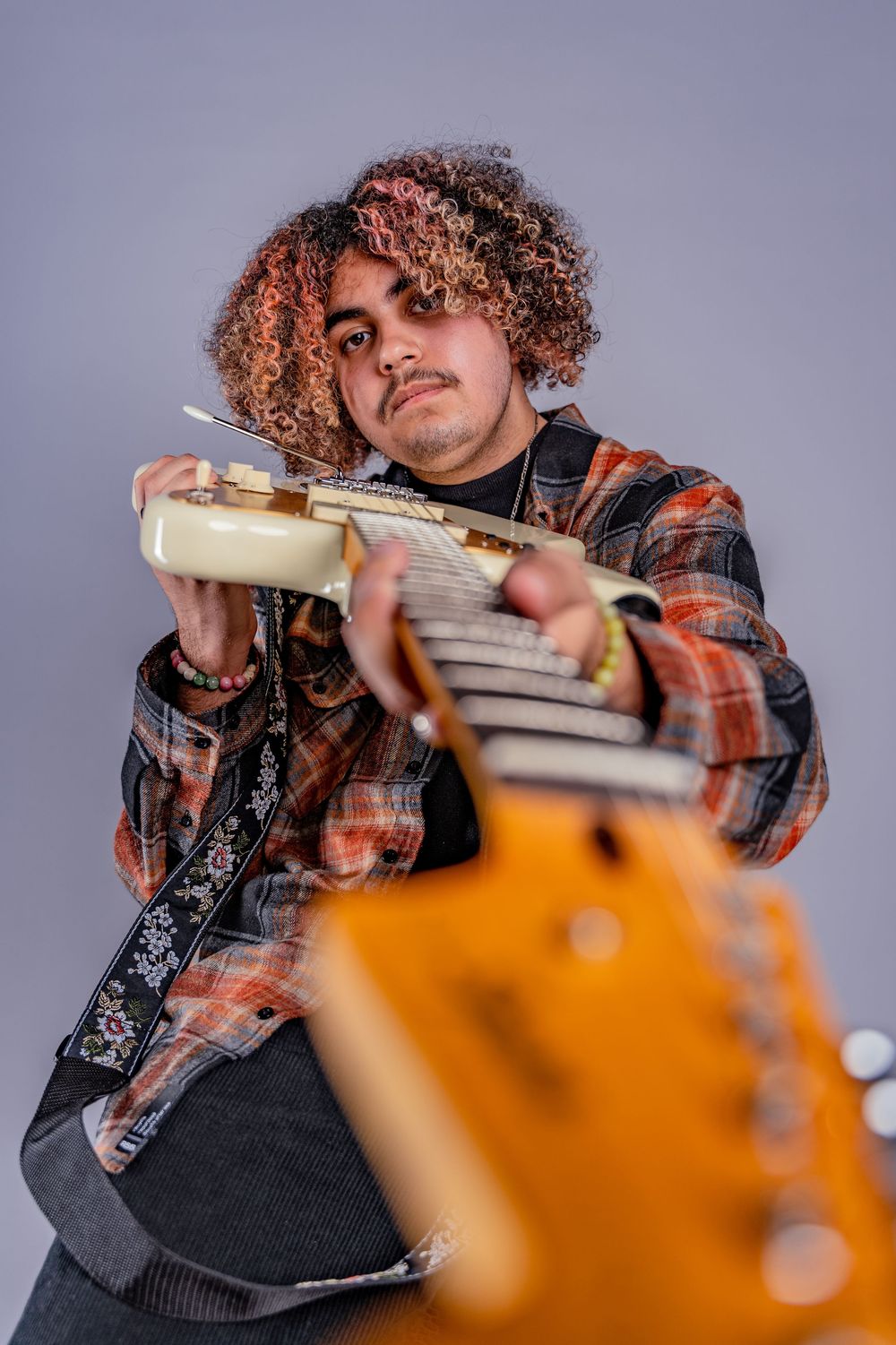Multiple angles of a musician playing electric guitar with curly hair and a plaid shirt against grey background.