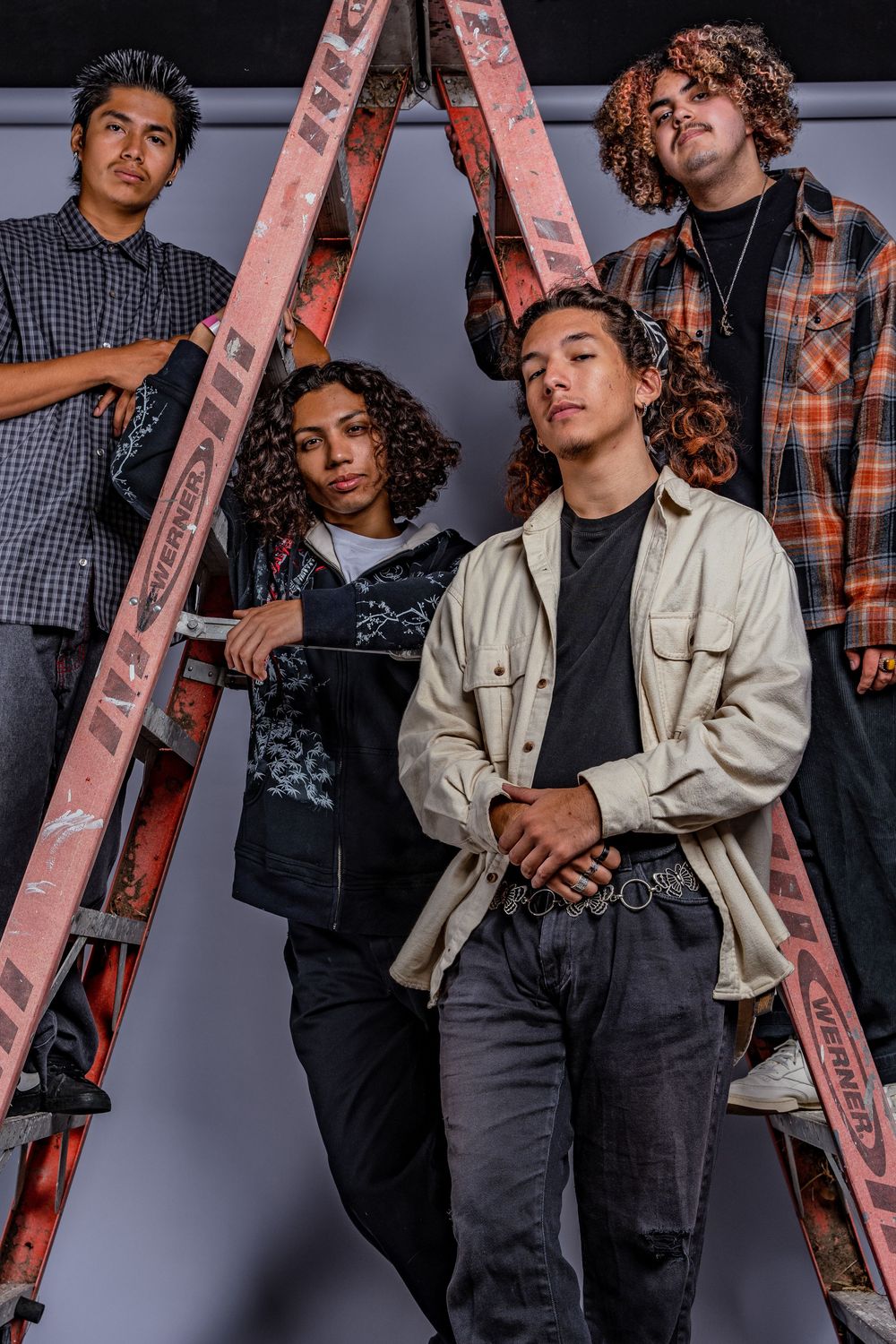 Band members in casual wear posing with instruments against pink ladder prop.