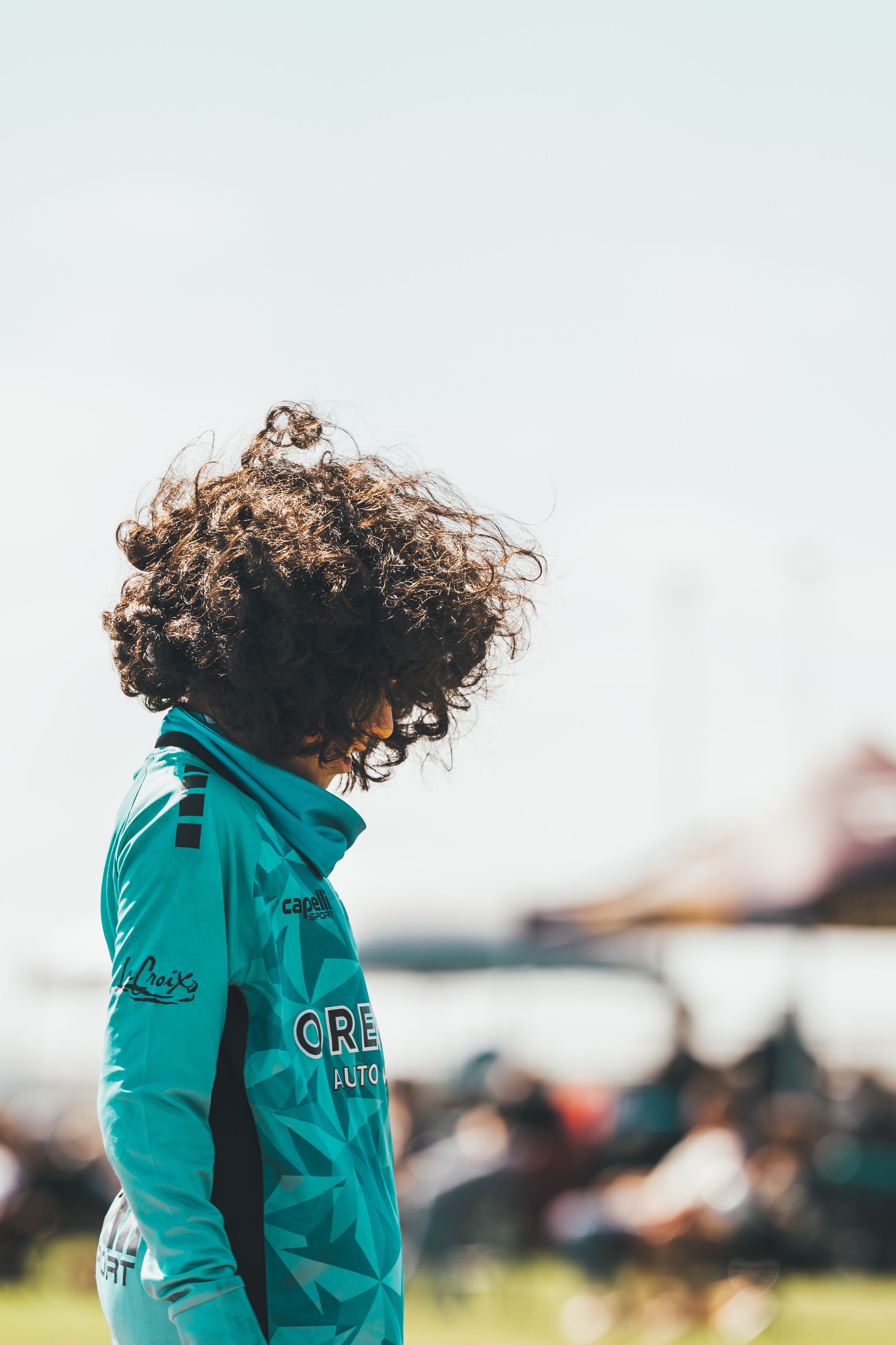 Soccer goalie in teal jersey with curly hair guarding his goal.