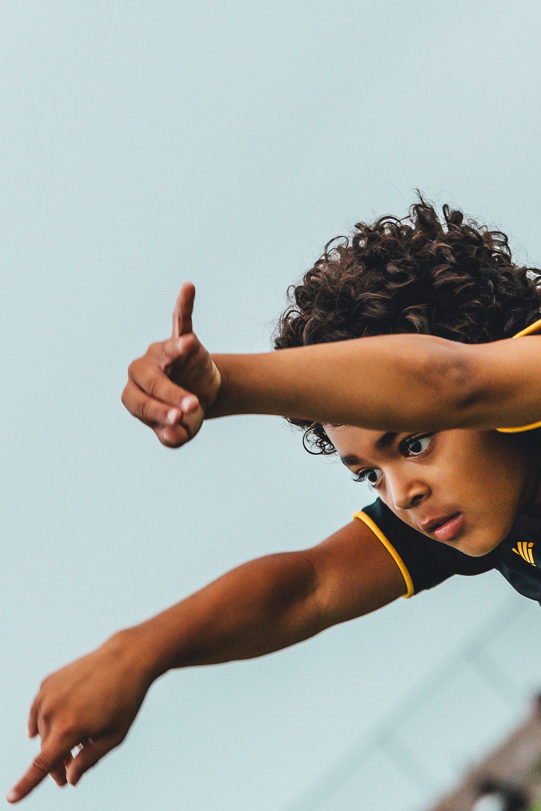Close-up of athlete with curly hair making pointing gesture against blue sky.