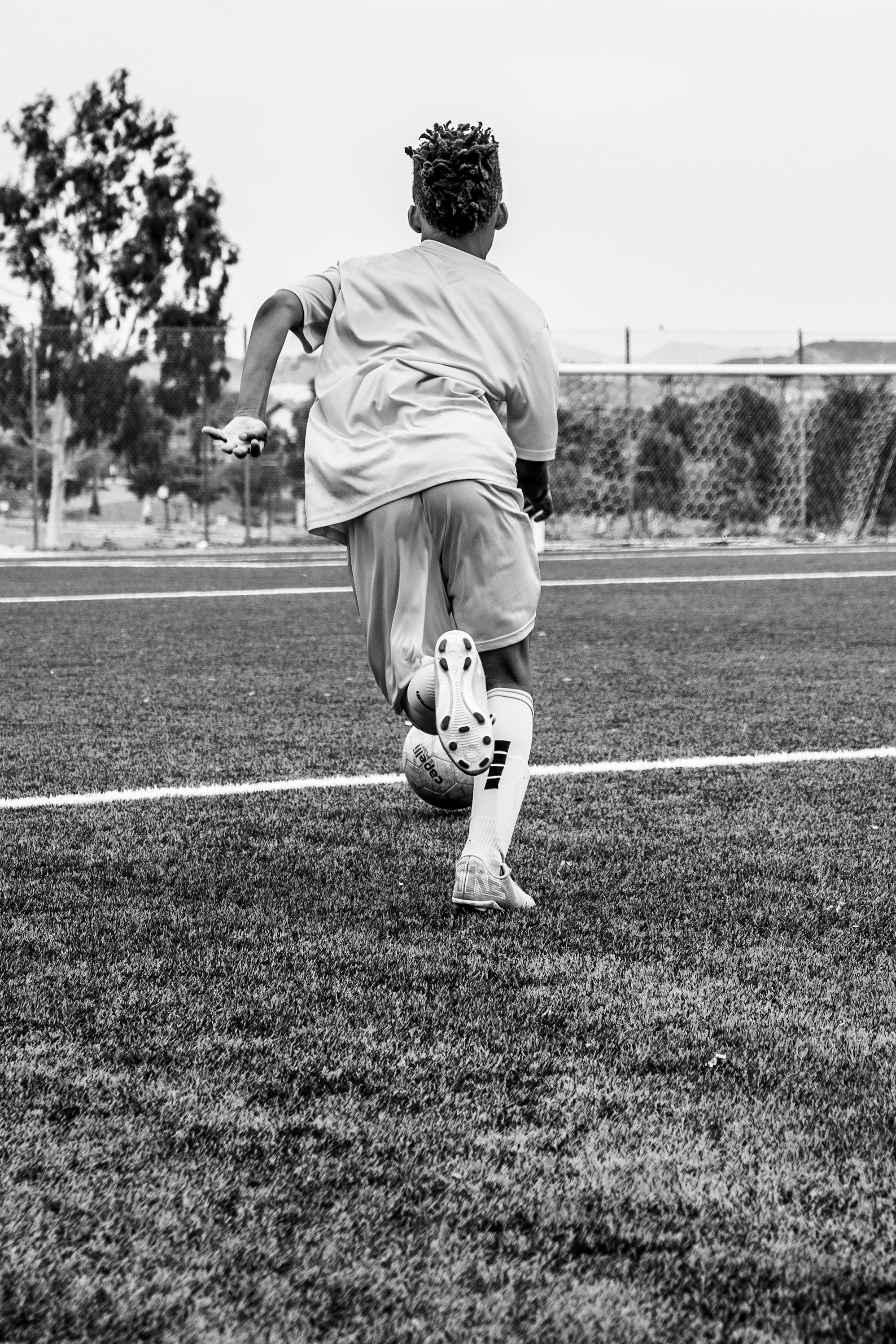Black and white photo of soccer player dribbling on grass field during game.