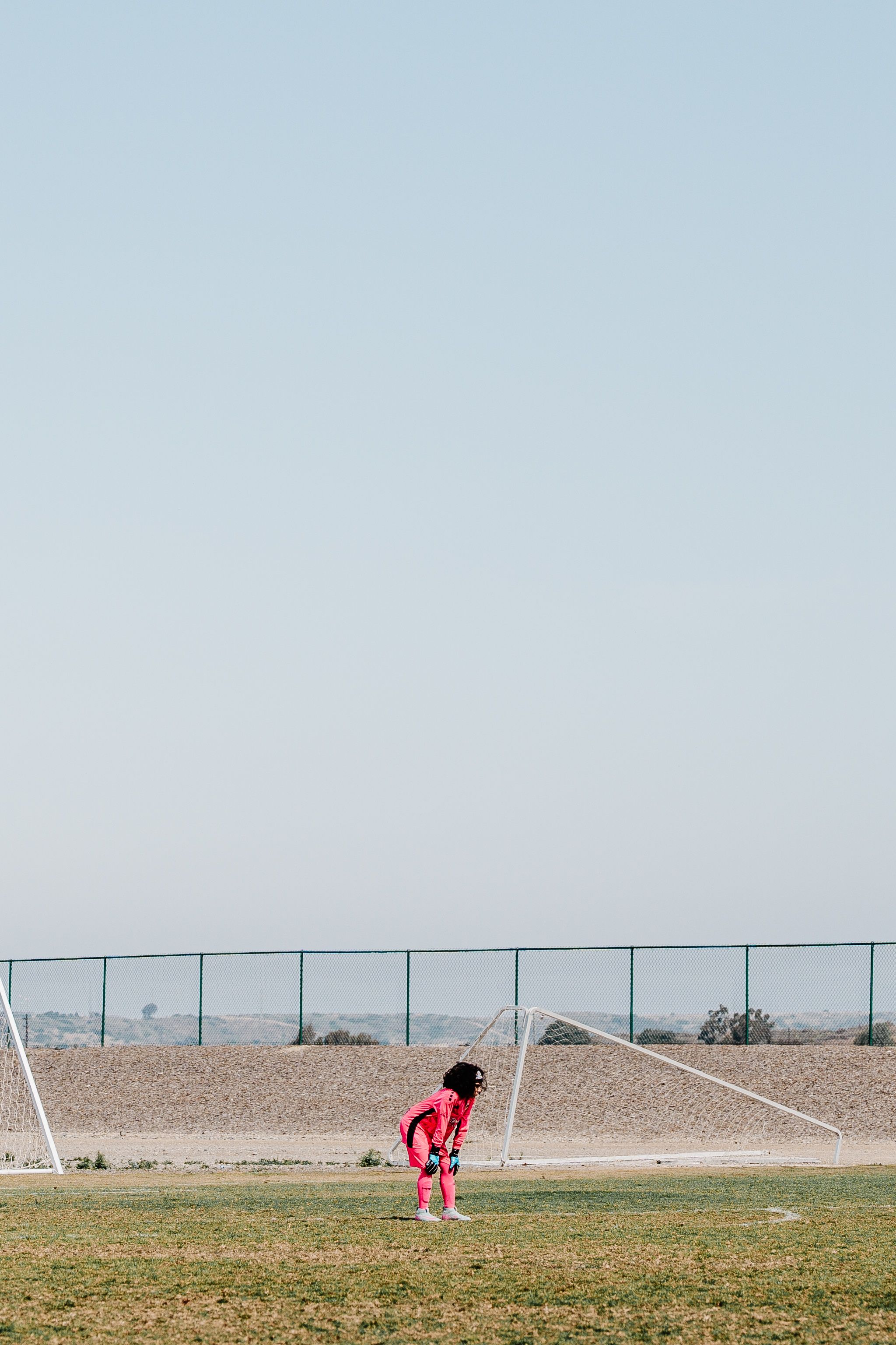 Soccer goal on grass field with player in red jersey standing in background.