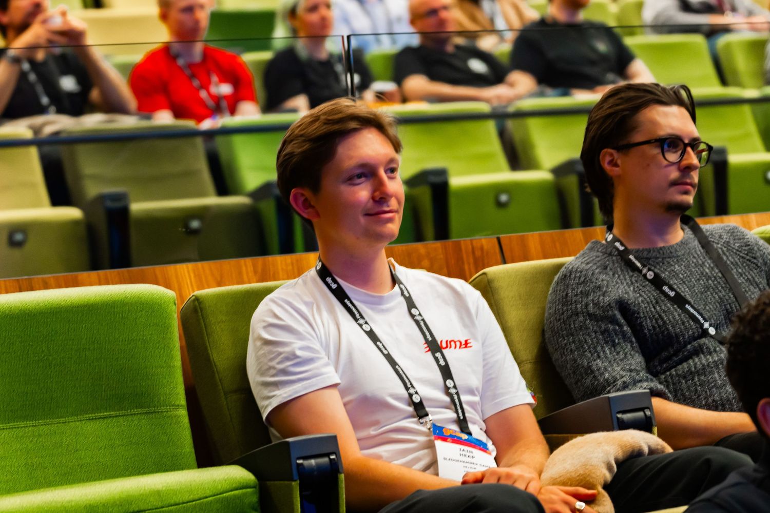 People sit attentively in rows of bright green chairs during what appears to be a conference or presentation.