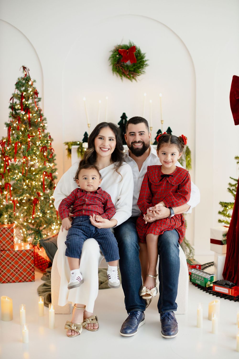 A festive Christmas photo series showing a family sitting together in front of decorated trees and holiday decor.