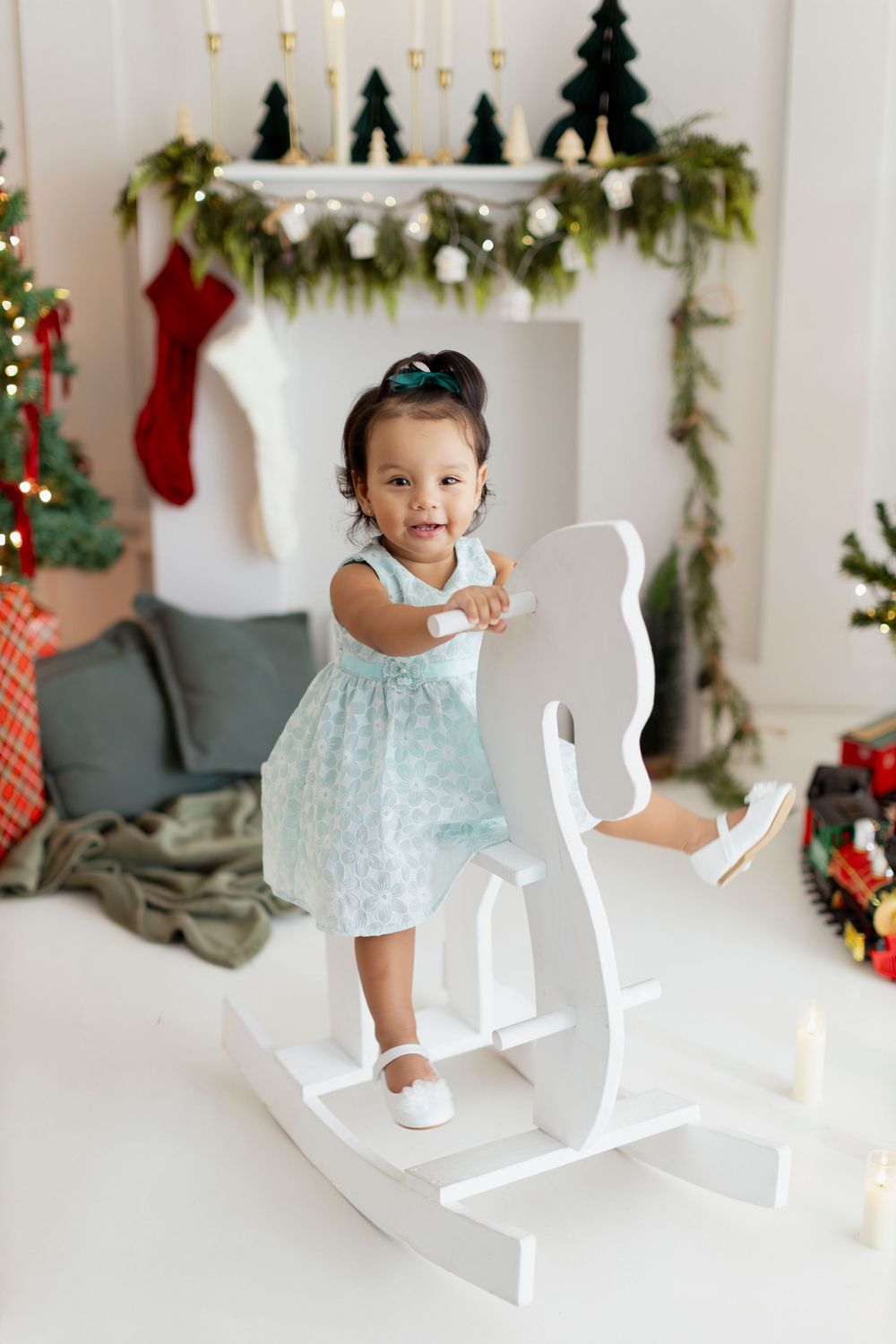 White wooden letters spell JOY in a festive holiday setting with garland and stockings decorating the background.