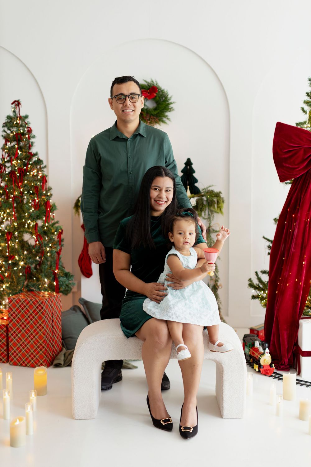 Holiday family portrait in white studio with Christmas trees, presents, and decorative arches.