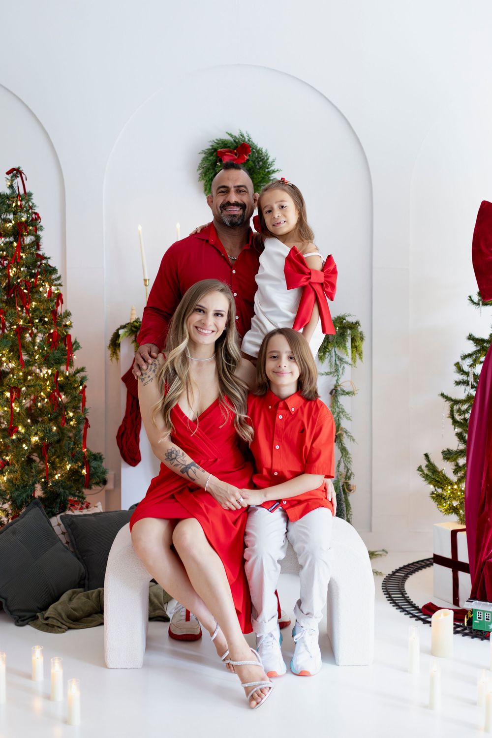 Family wearing matching red and white outfits poses together for Christmas photos in front of decorated tree.
