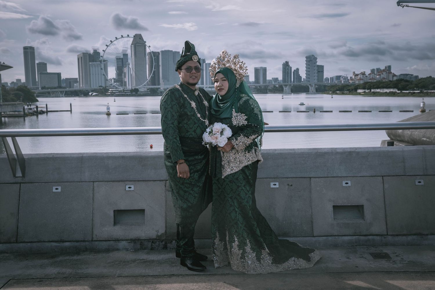 Couple in matching green attire pose against city skyline backdrop during overcast weather.
