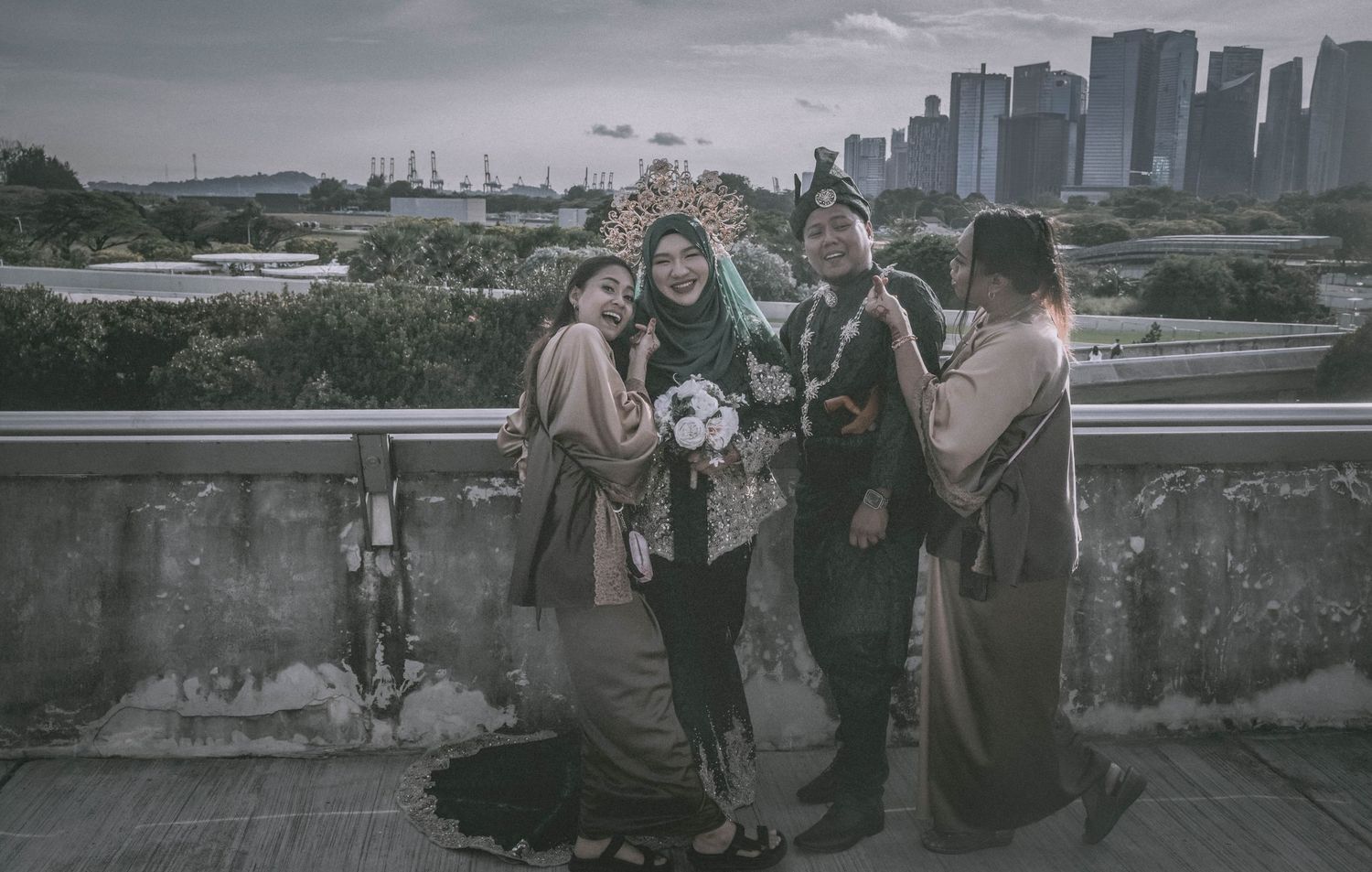 Wedding party poses for photos on rooftop with urban cityscape visible in background.