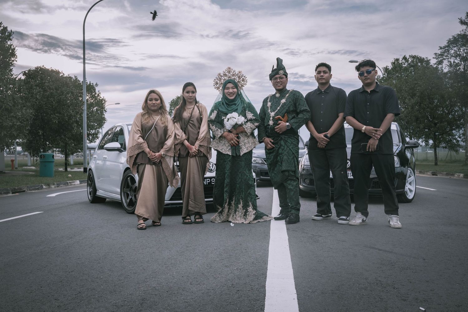 Group photo of wedding party members posing on a street with a car in the background.