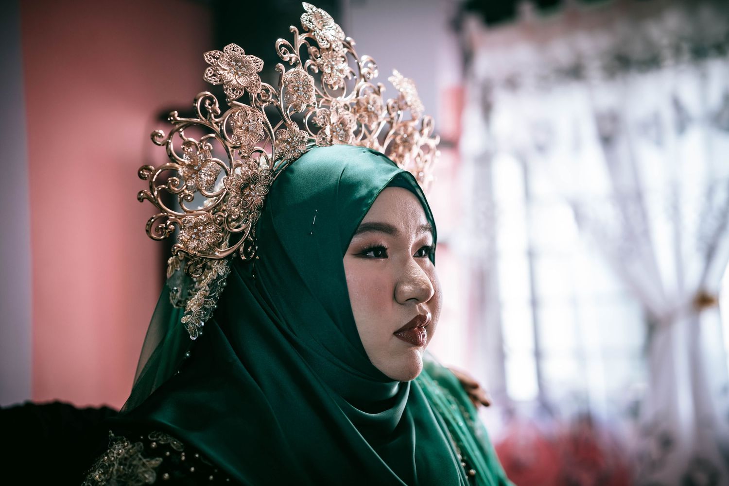 Side profile of someone wearing an emerald green hijab adorned with an ornate golden crown.
