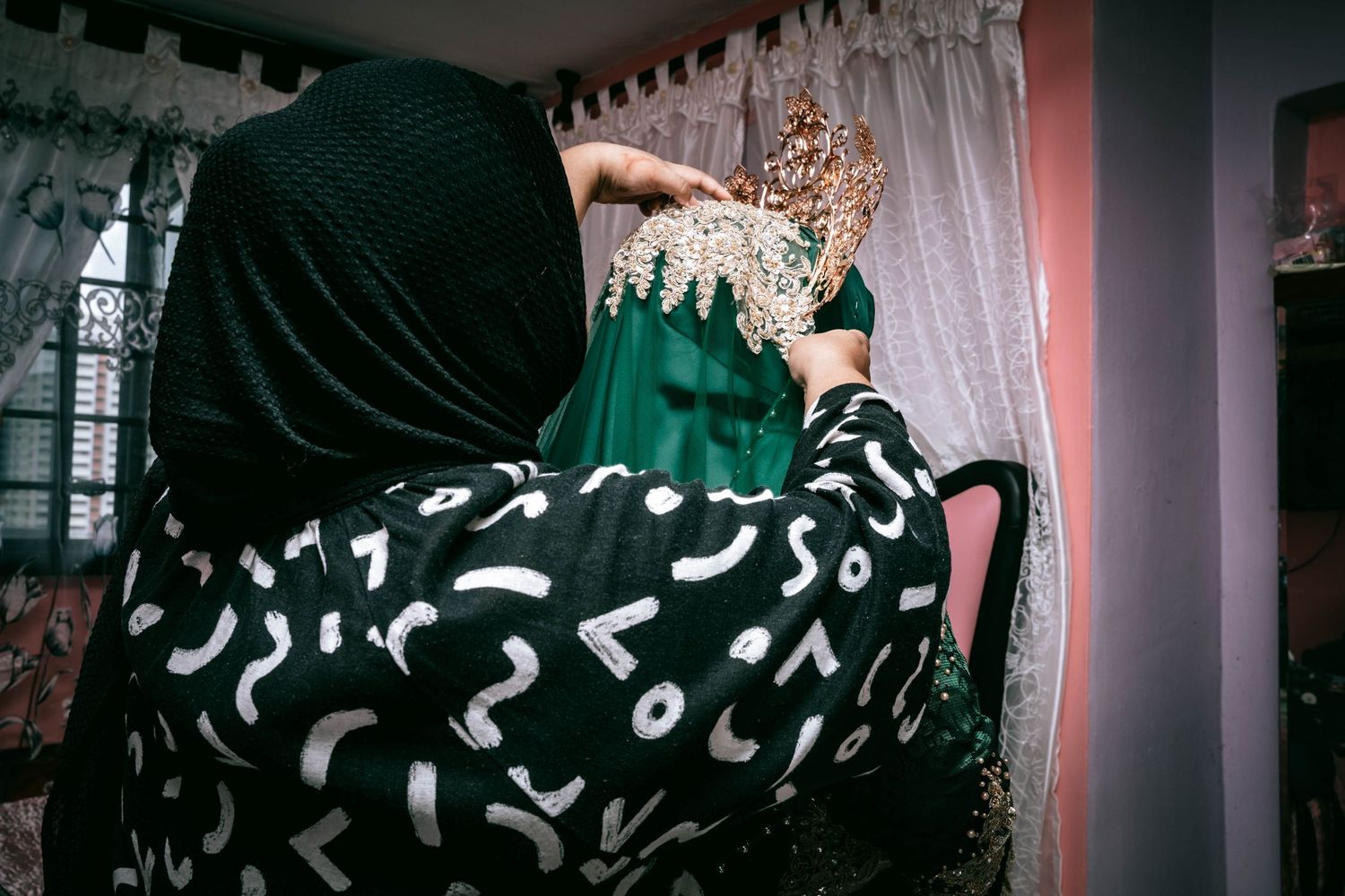 Person in patterned black dress adjusts decorative crown at cultural celebration.