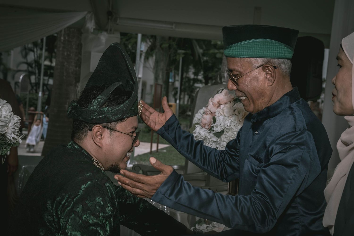 Traditional blessing ceremony with elder in green cap during Malay wedding.