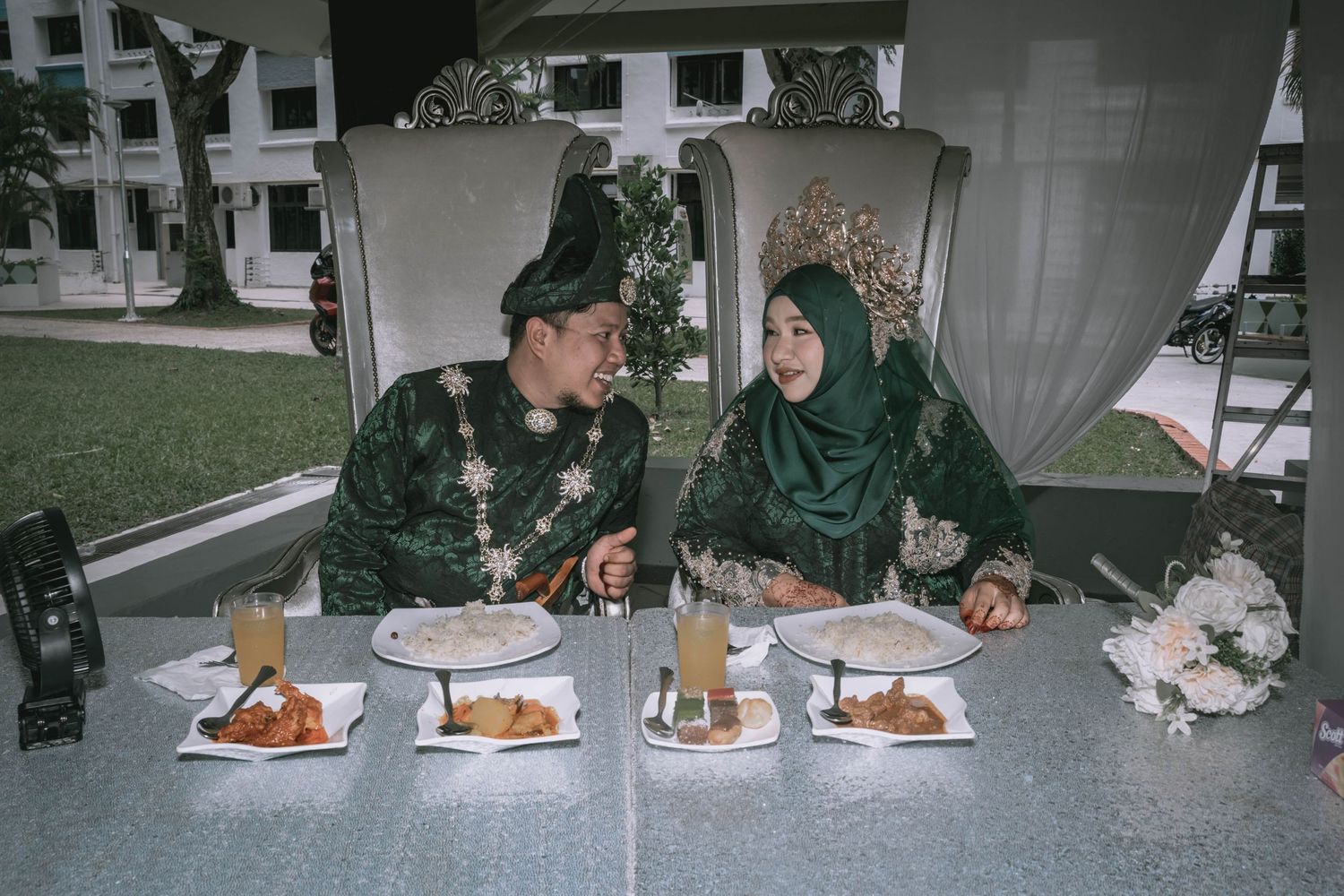 Couple in matching green outfits sharing a meal together at an outdoor setting with multiple plates of food.