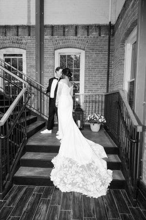 A black and white photo of newlyweds on a brick porch with a dramatic wedding dress train.