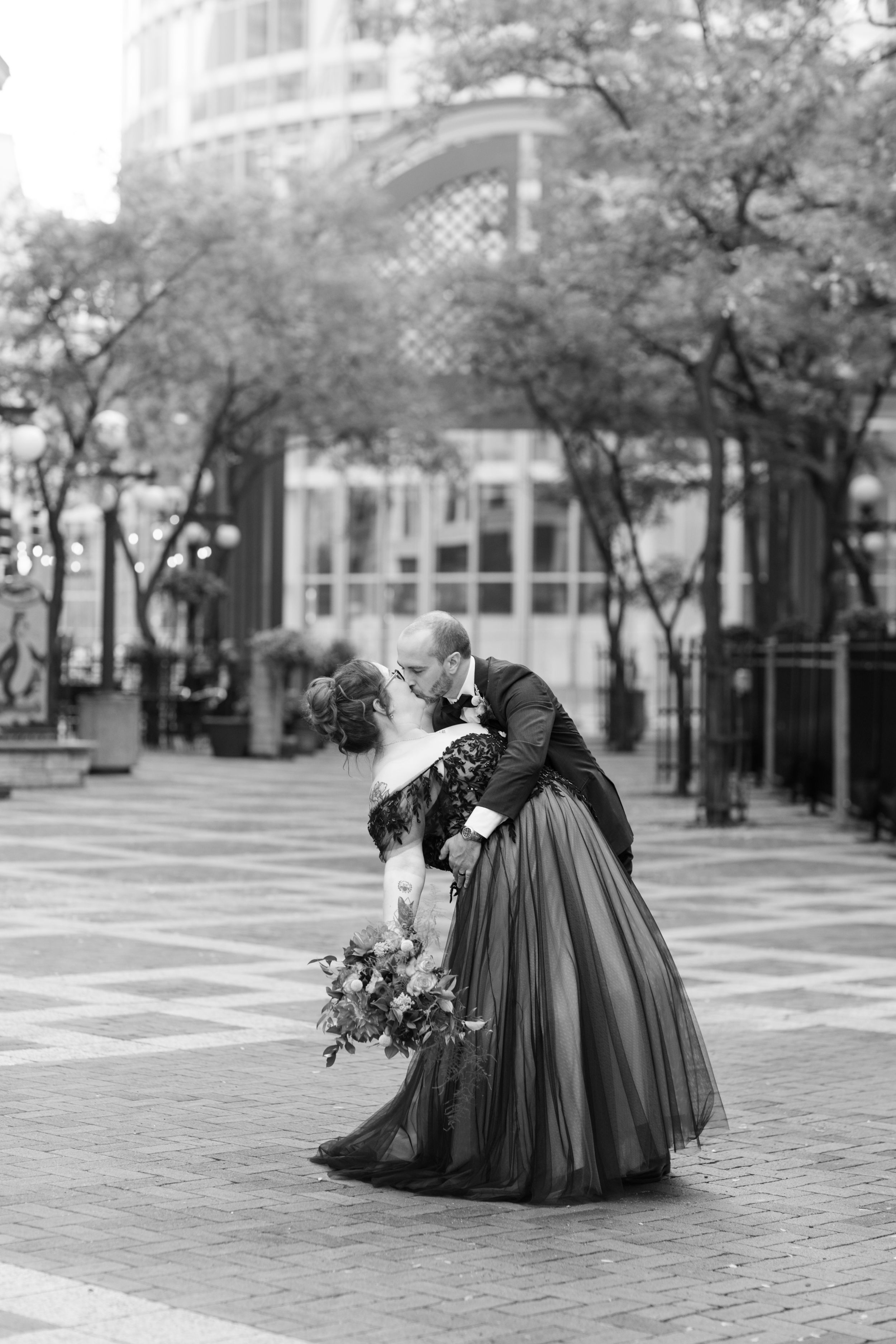 A romantic dip pose of a couple in formal wear on a brick-paved city plaza.