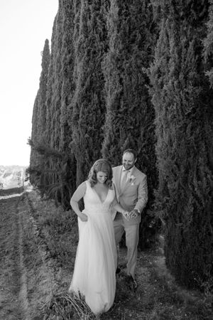 A wedding couple shares a joyful moment against a backdrop of tall cypress trees.