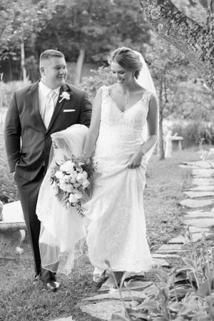 A couple walking together on a garden path in elegant wedding attire.