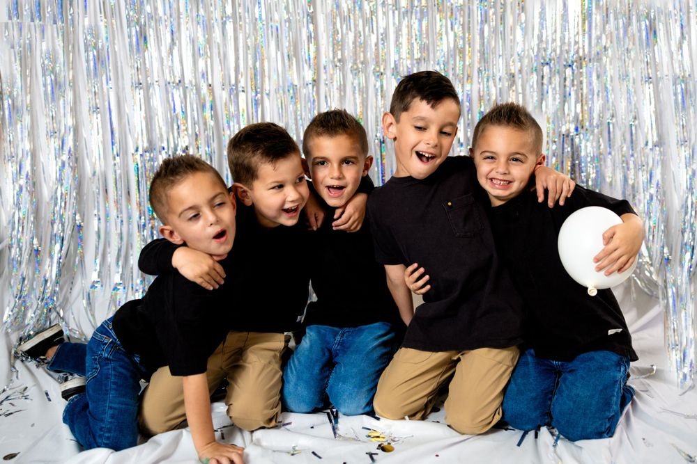 Boys in matching outfits pose playfully against silver tinsel backdrop.