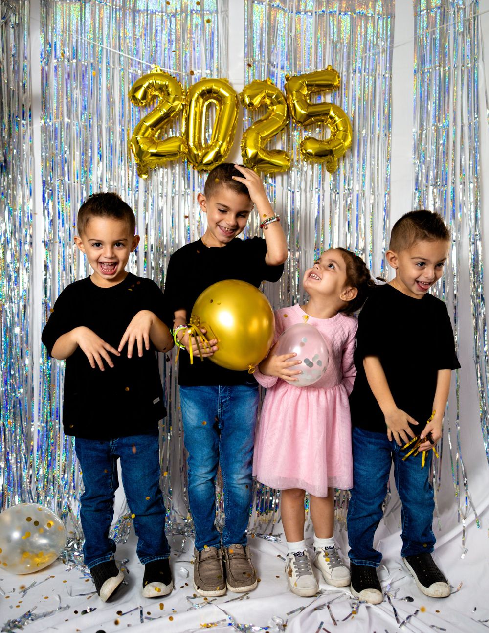 Four children pose against a silver backdrop with gold 2025 balloons and festive decorations.