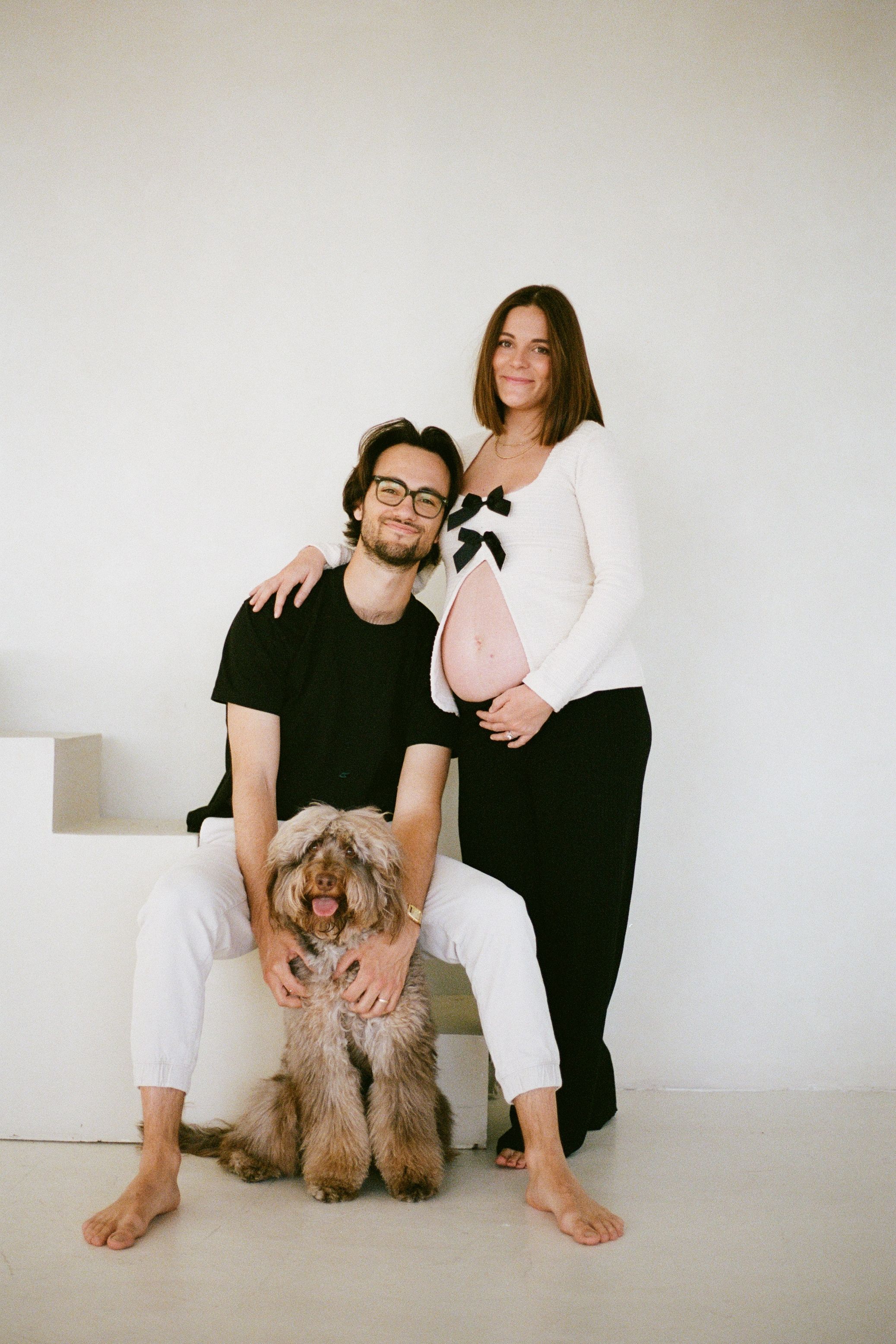 A couple poses with their fluffy brown dog in a bright white studio setting.