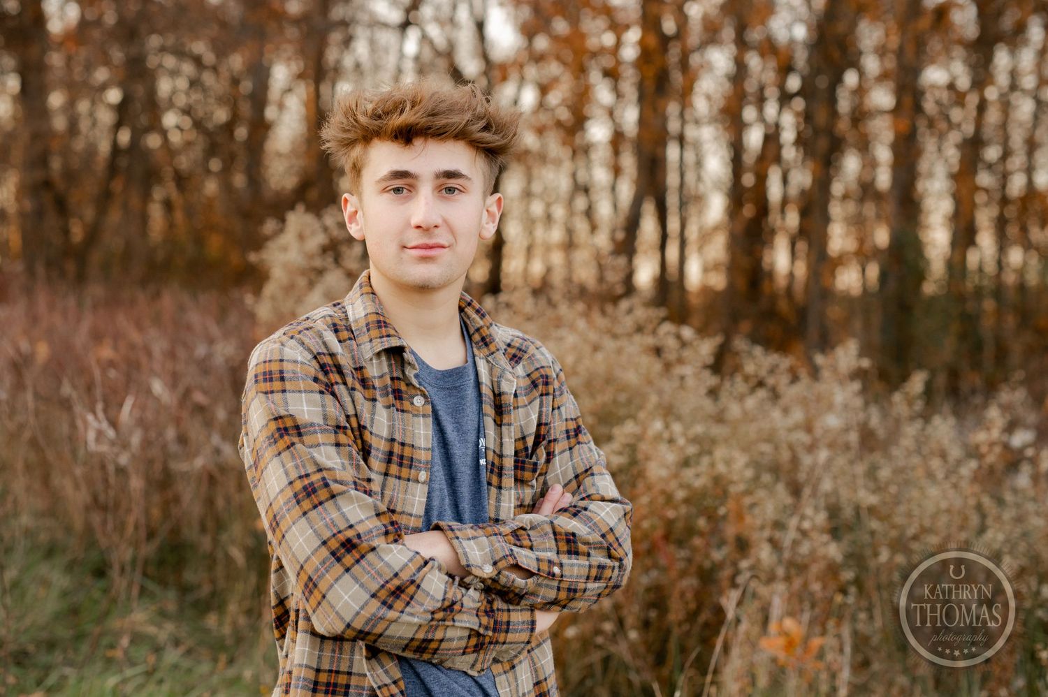 A casual portrait of someone in plaid clothing against a backdrop of fall foliage.
