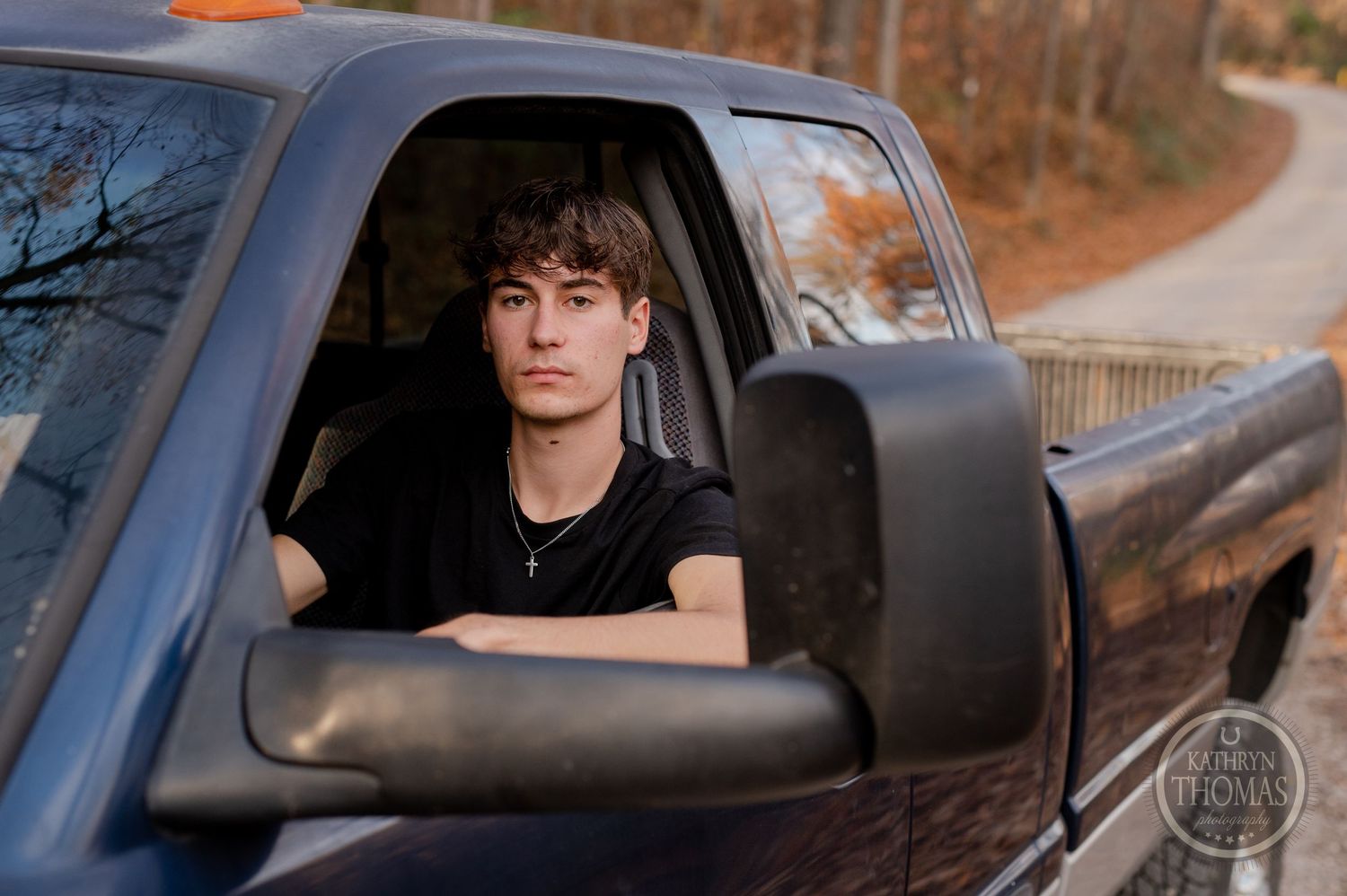 View through driver's side window of dark Ram pickup truck in wooded setting.