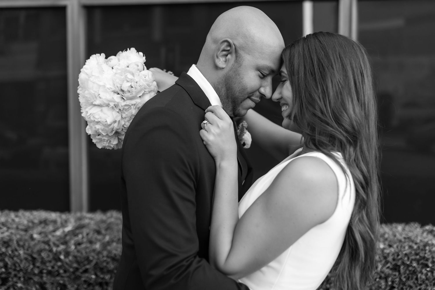 A timeless black and white portrait of newlyweds sharing an intimate moment with white bouquet.