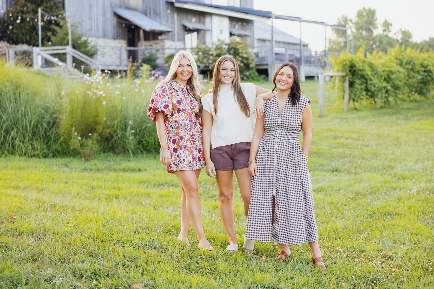 Boutique models gathering on a sunny grassy field near a barn building.