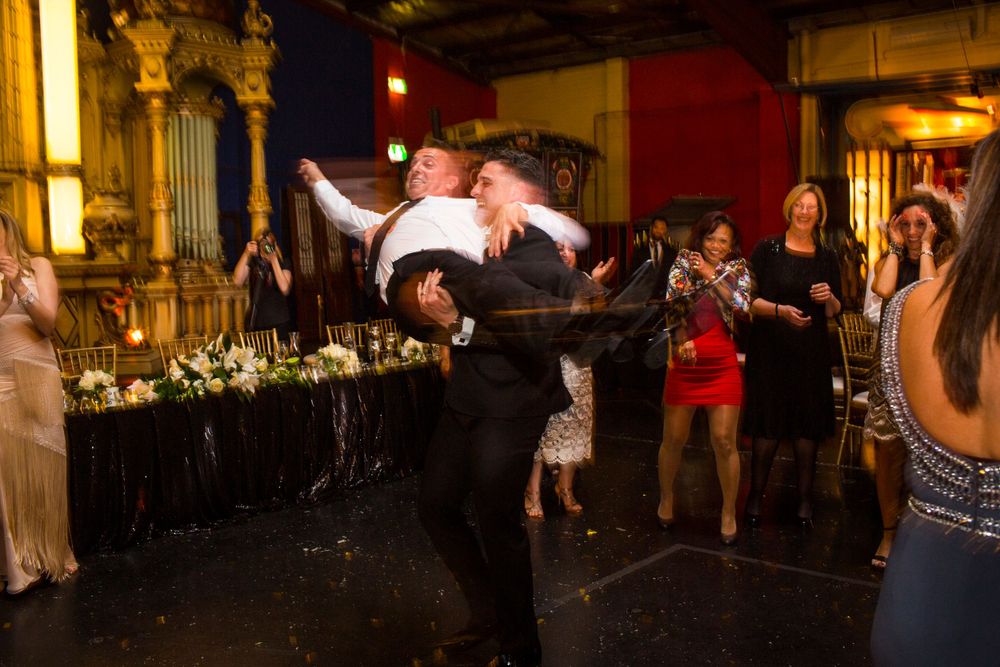 Couple performing dramatic dance lift during wedding reception in ornate venue.