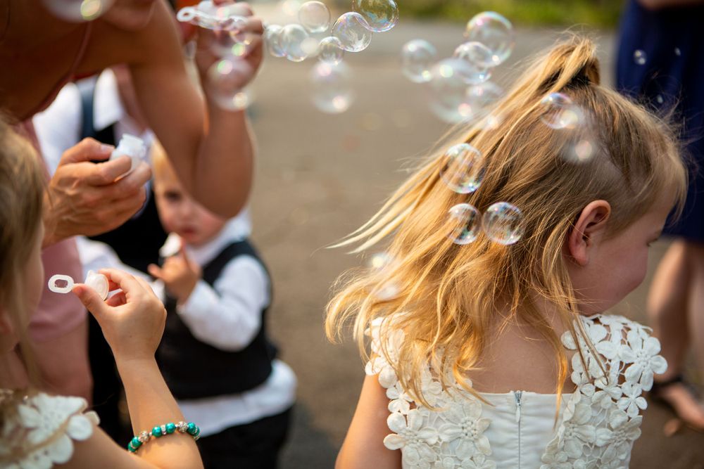 Two figures blowing bubbles outdoors with a person's blonde hair catching the sunlight.