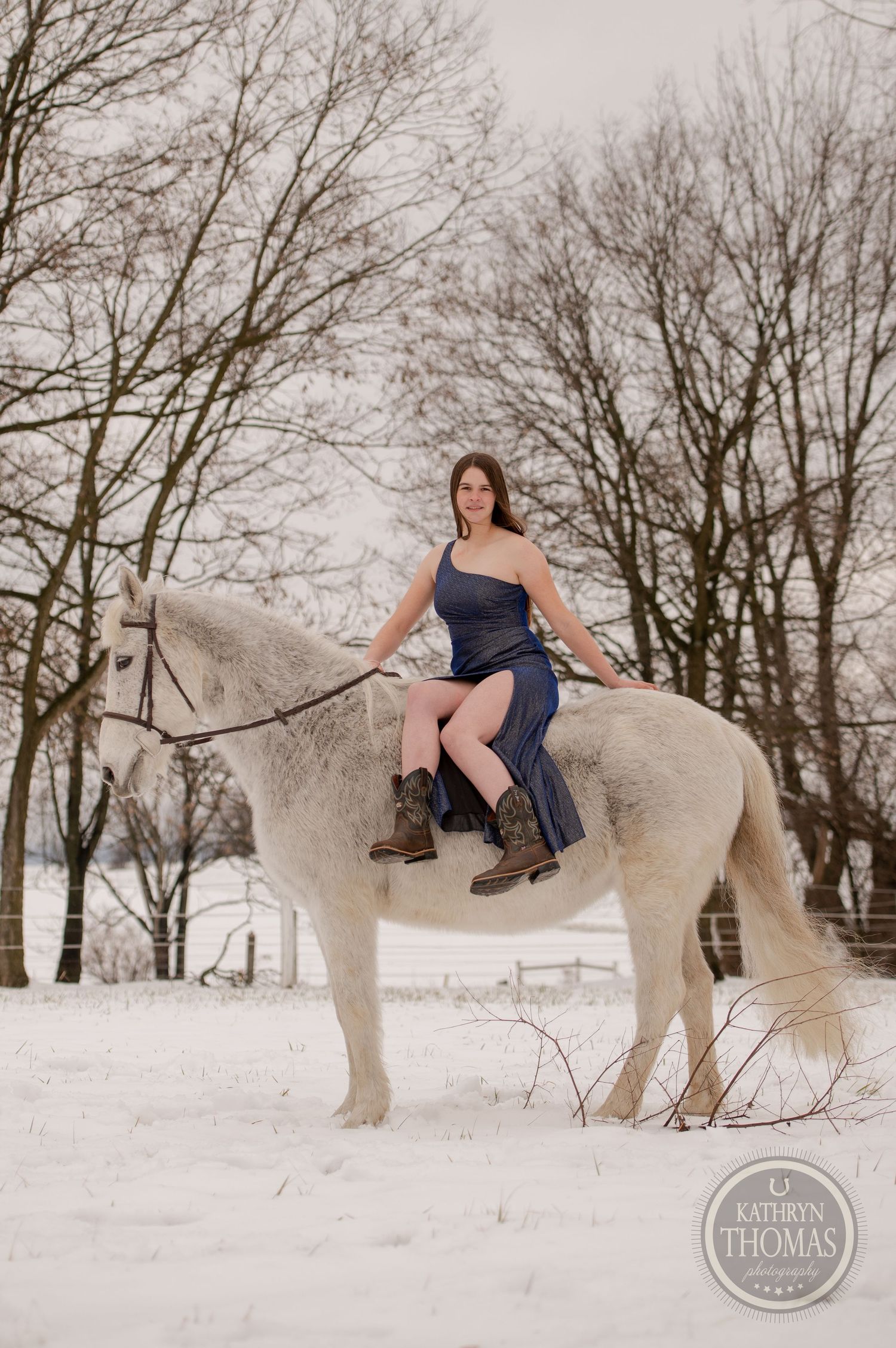 A person riding a white horse in a winter setting with bare trees.
