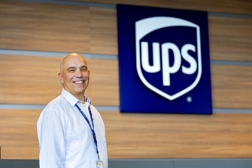 A professional stands in front of a UPS corporate logo on a modern office wall.