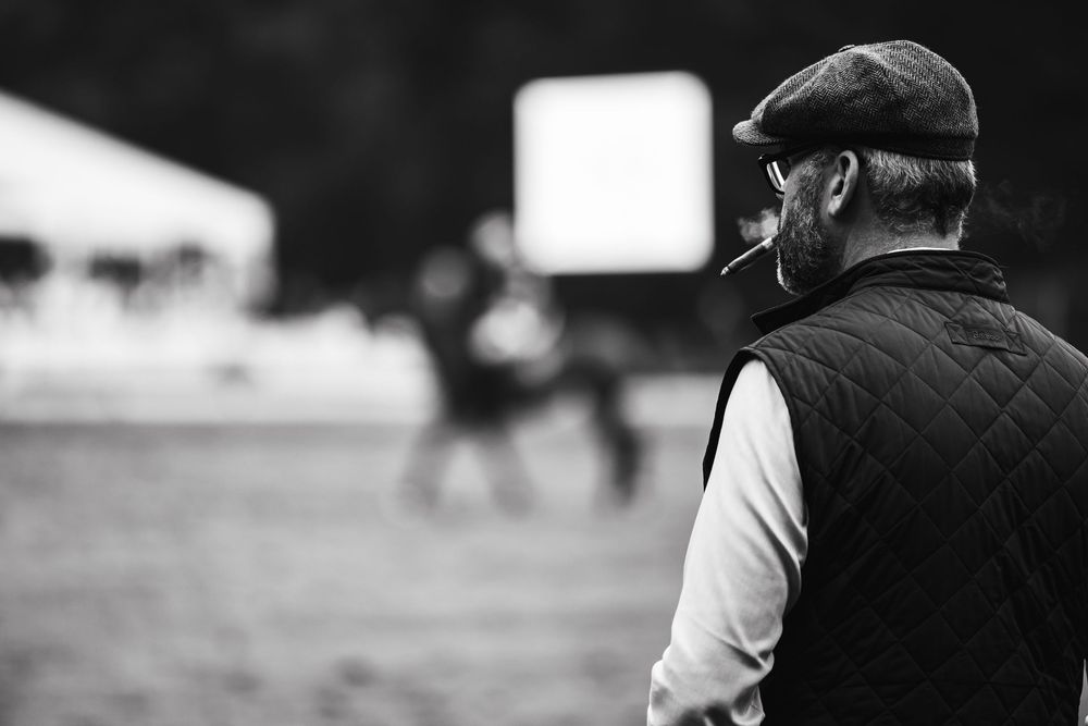 Black and white image of someone in a quilted vest and cap watching from the sidelines.