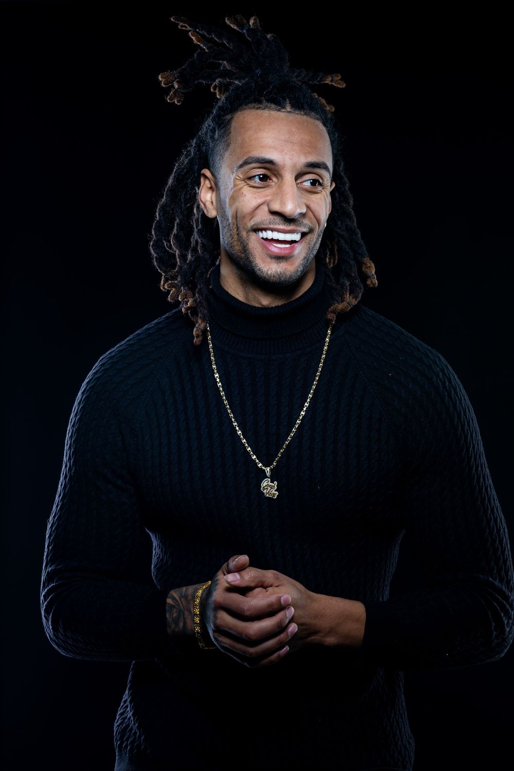 Portrait series against black background showing person in dark sweater with gold necklace in various poses. Jay Francis