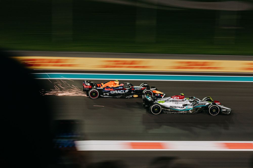 Two Formula 1 race cars engaged in a high-speed battle during a night race with motion blur effects in the background.