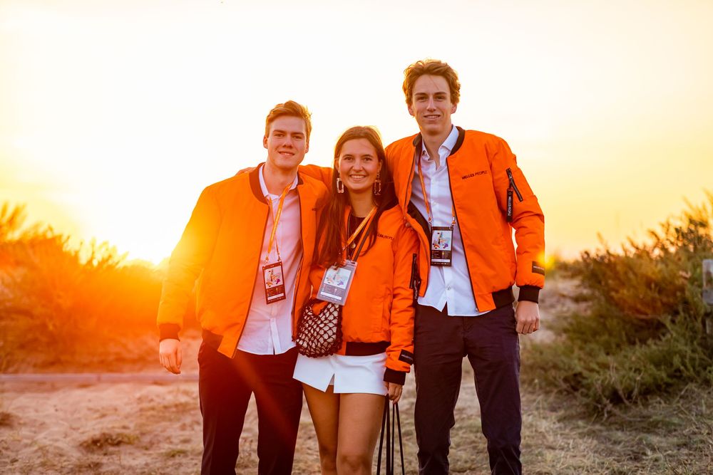 Three people wearing matching orange attire pose together at sunset.