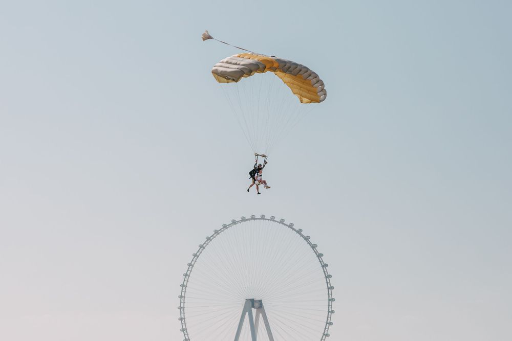 A parachuter glides through the sky above a large Ferris wheel structure on a misty day.