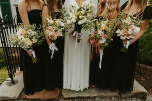 Wedding party holding elegant white and peach floral bouquets against black dresses.