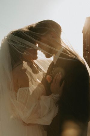 Romantic silhouette of wedding couple sharing an intimate moment in sunlit veil.