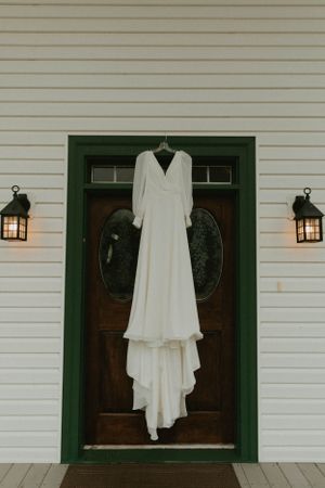Classic white wedding dress hanging on wooden door with lantern sconces.
